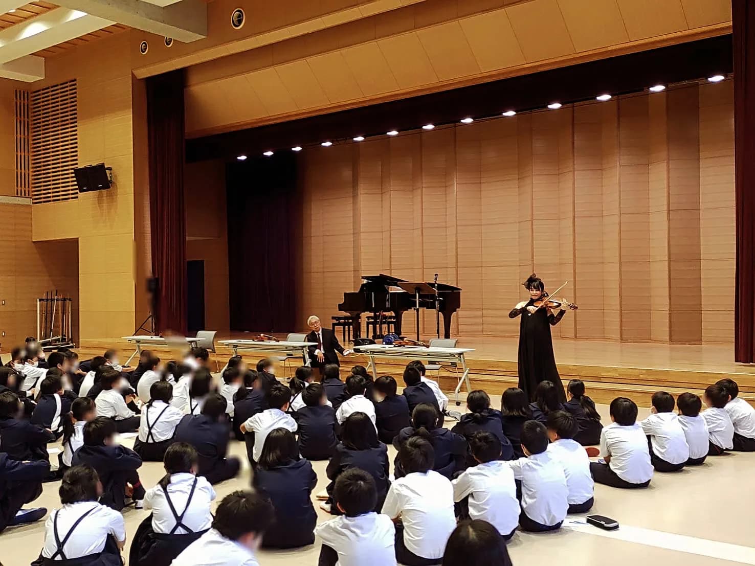 体育館で児童の前でヴァイオリンを演奏する田中雅子（児童の顔は撮影時よりモザイク処理済み）